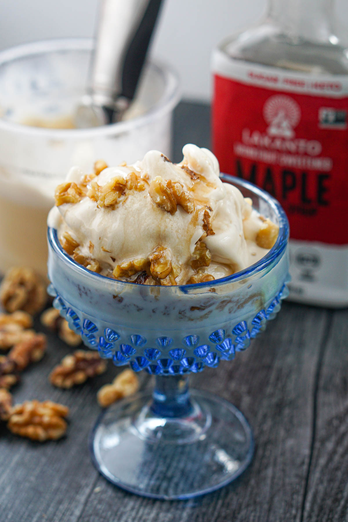 blue glass dish with maple ice cream with maple syrup and walnuts