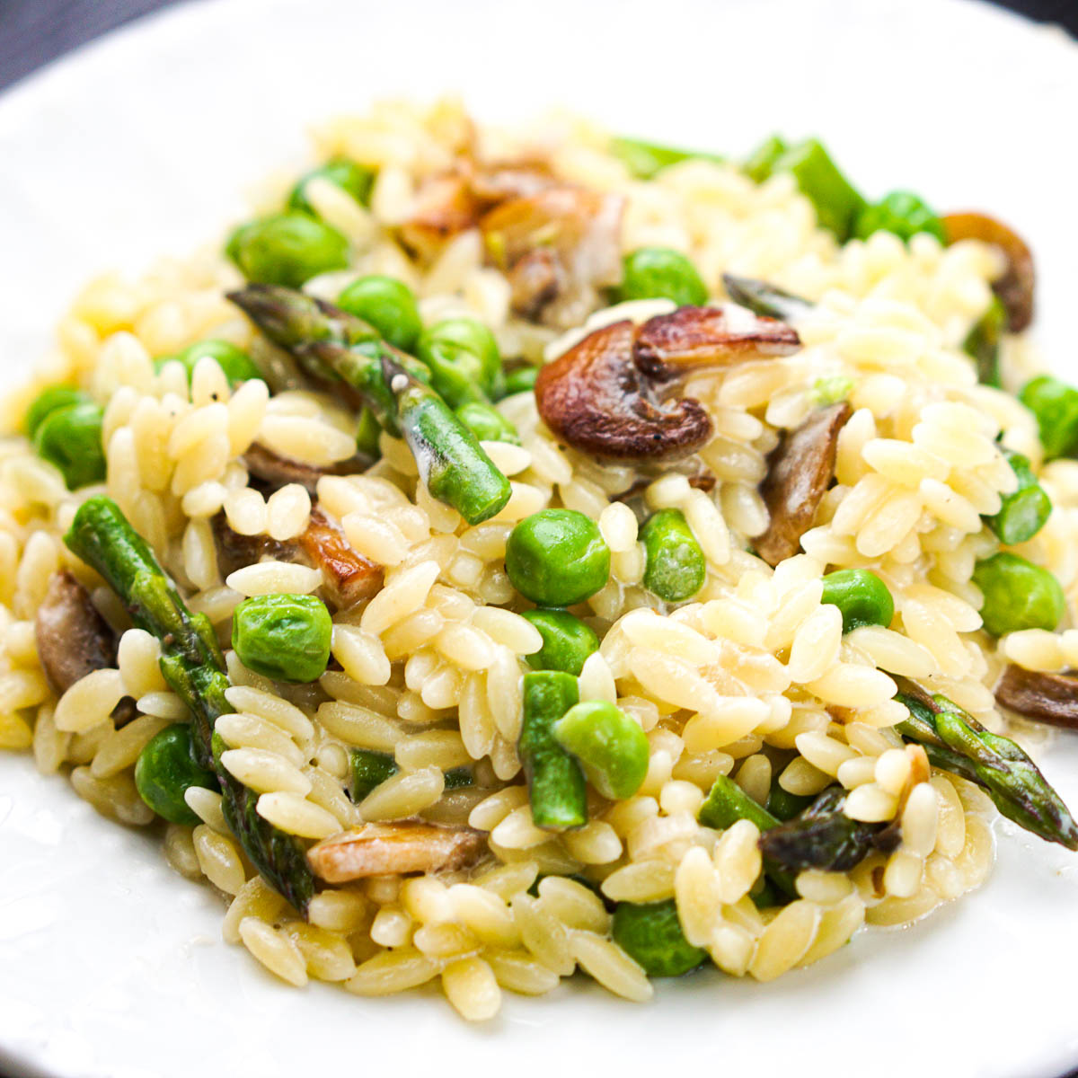 closeup of orzo with peas and mushrooms on white plate