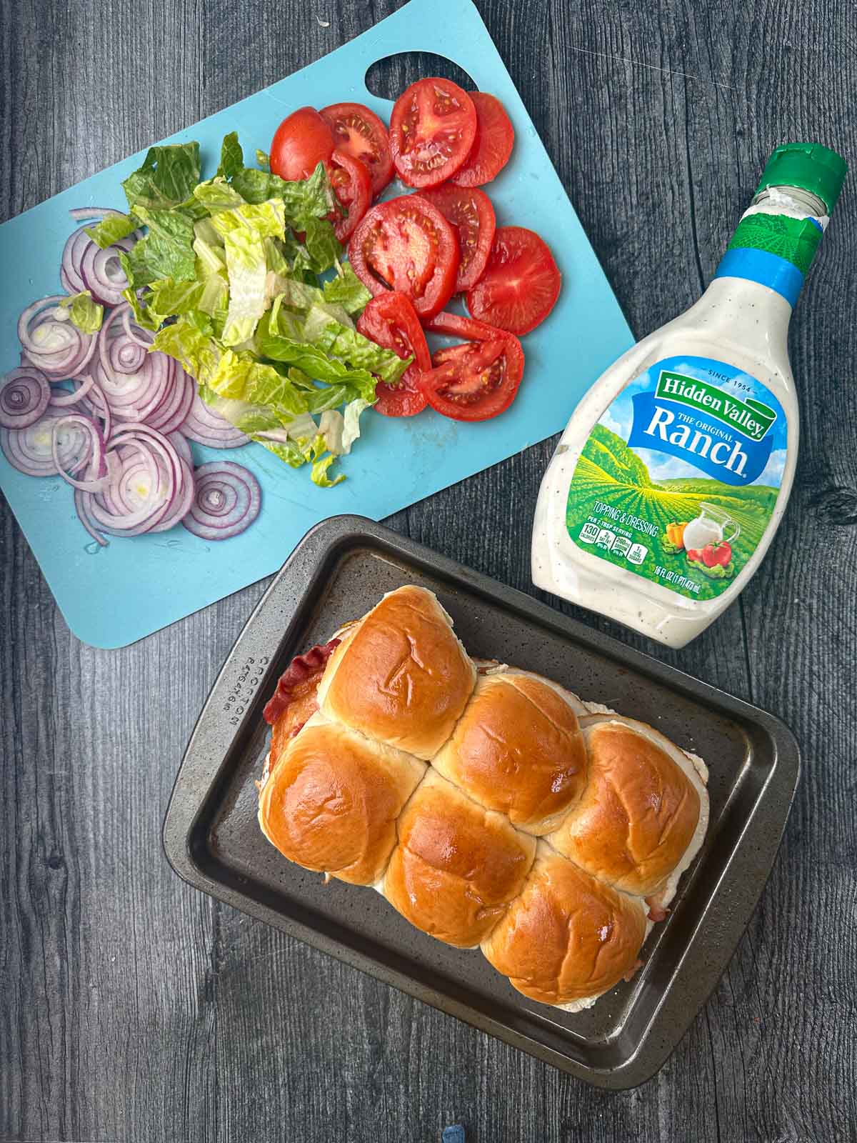 aerial view of sliders on baking tray and sliced veggie toppings  and ranch dressing