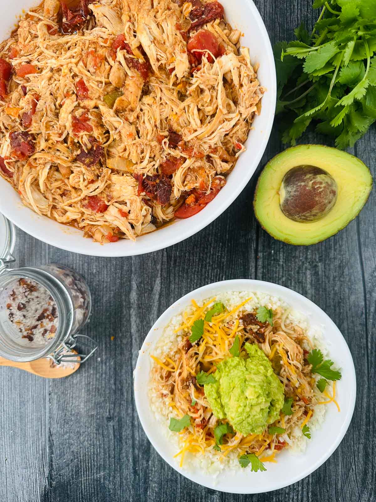 aerial view of white bowl and plate with shredded chipotle chicken and avocado and cilantro