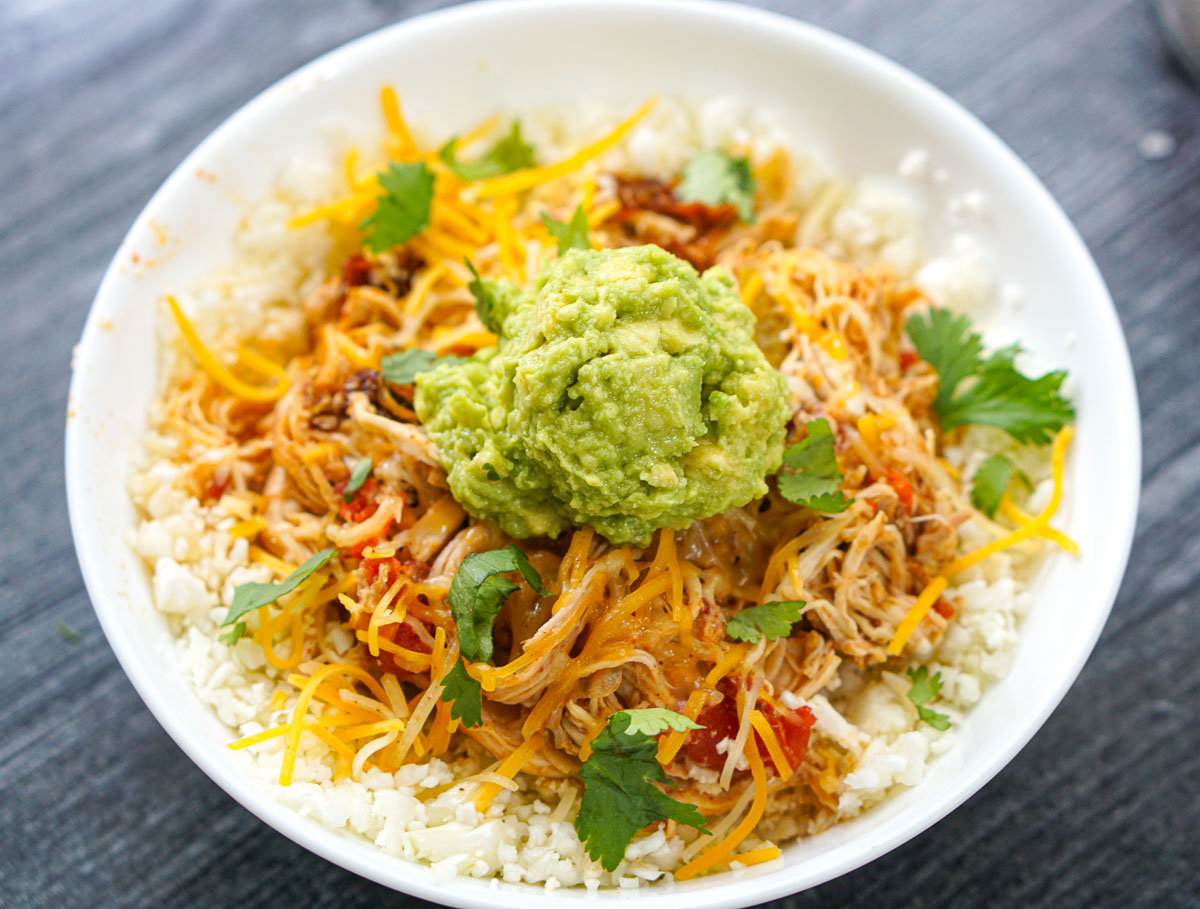 white bowl with cauliflower rice topped with shredded chicken and topped with mashed avocado