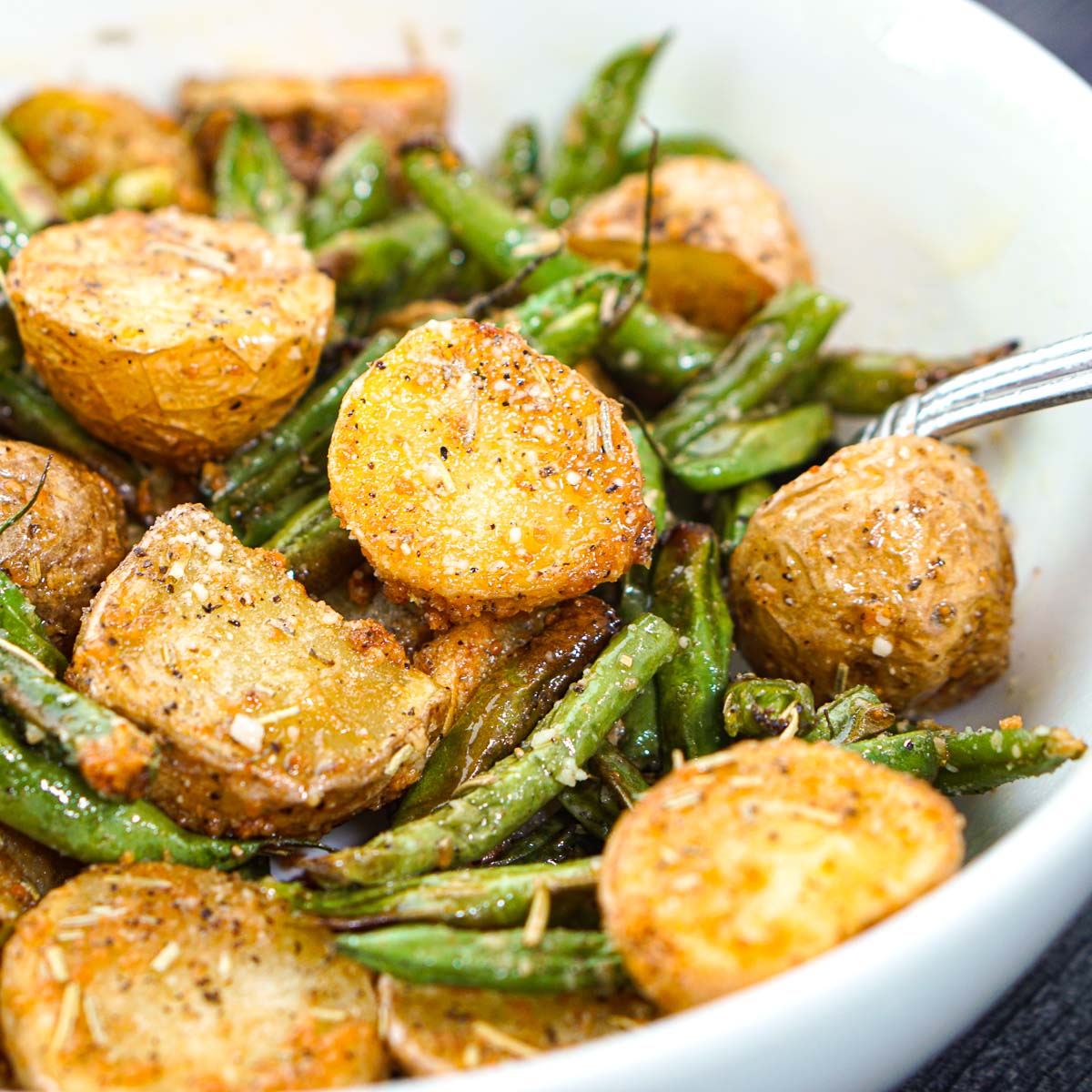 closeup of white bowl with air fryer parmesan potatoes and green beans