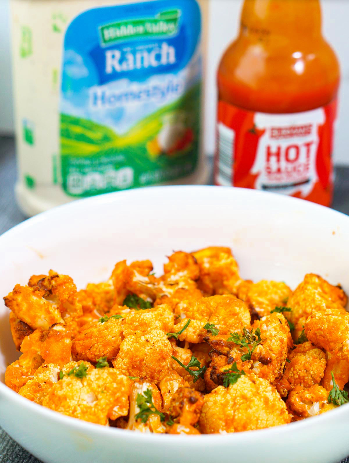 closeup of a bowl of buffalo cauliflower and bottles in the background