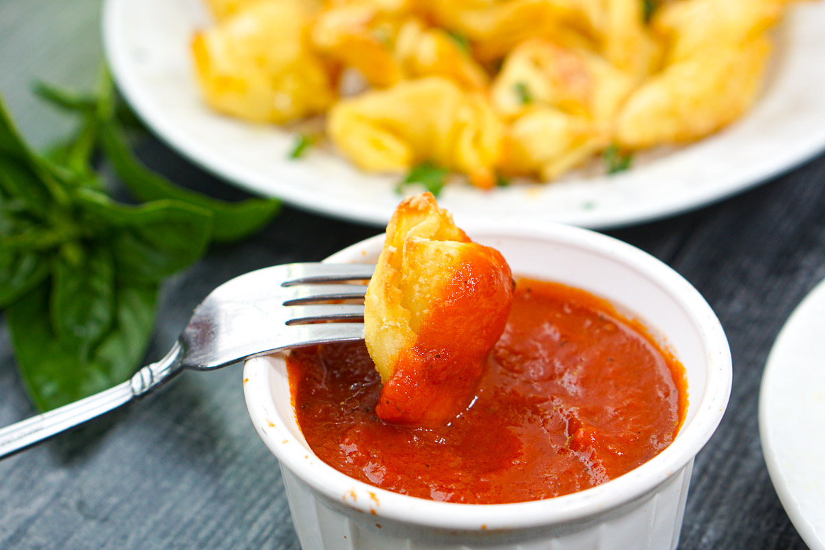 a fork dunking a tortellini in sauce
