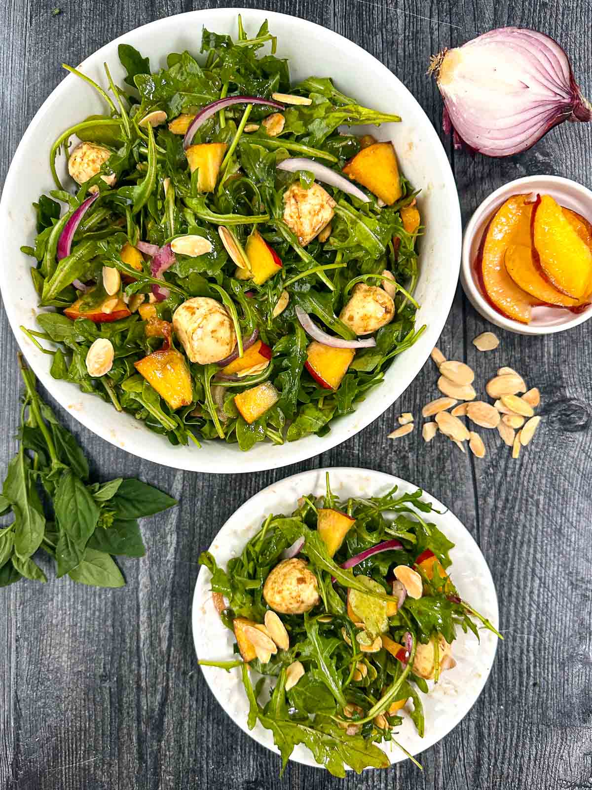 aerial view of a white bowl and plate with peach arugula salad and various ingredients