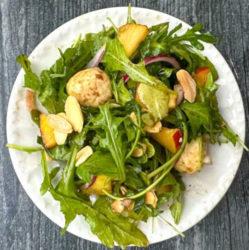 white plate with peach arugula salad with almonds and fresh mozzarella