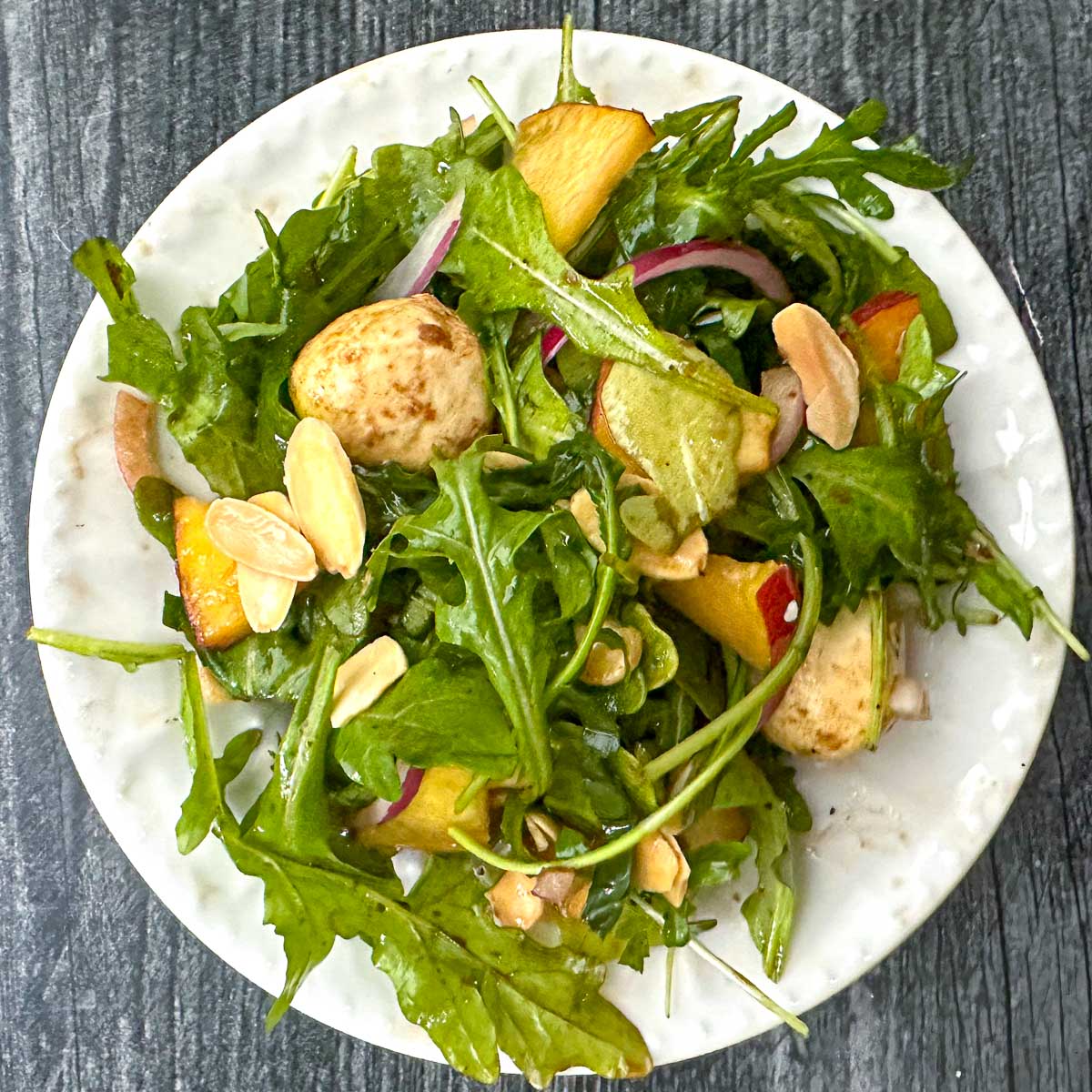 white plate with peach arugula salad with almonds and fresh mozzarella