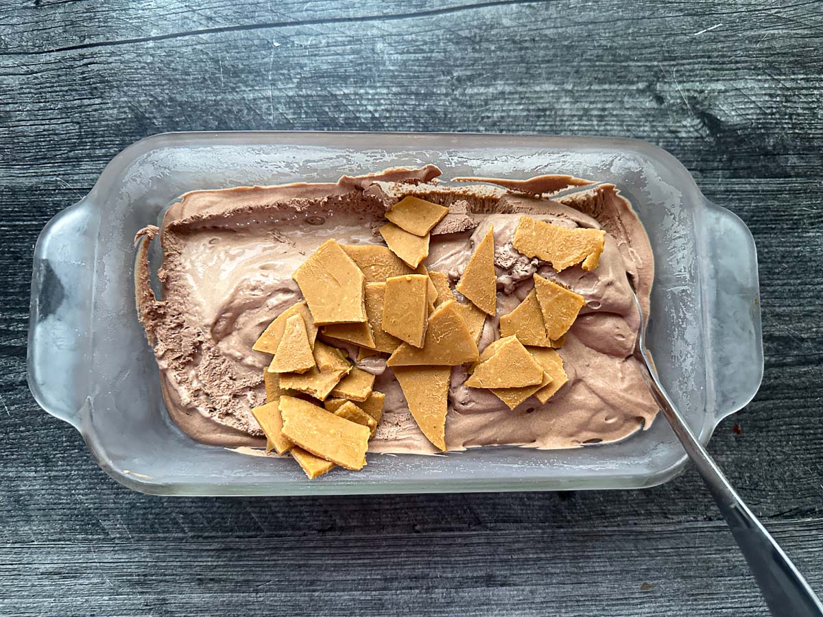 Bread loaf dish with the ice cream mixture and peanut butter pieces on top.