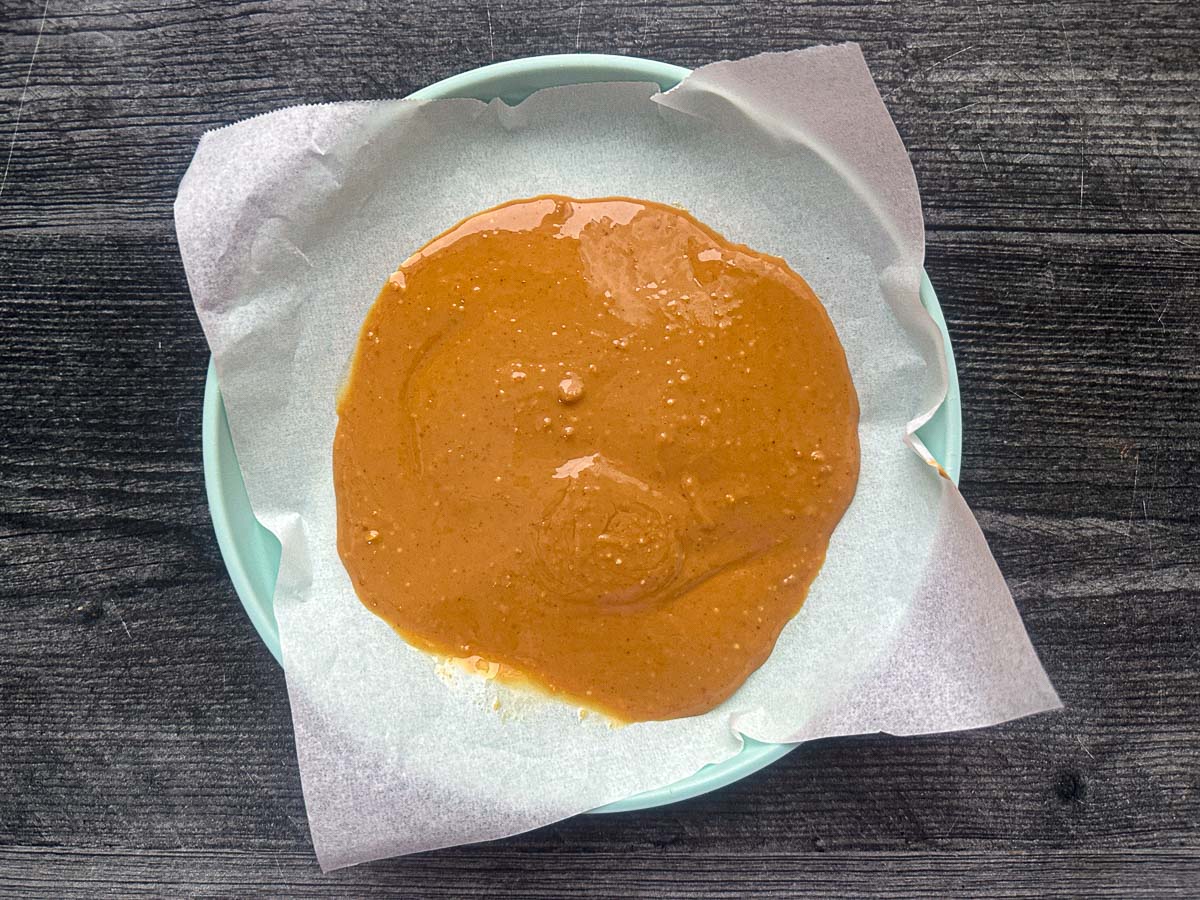 Plate with a piece of parchment paper and peanut butter spread in an even layer.