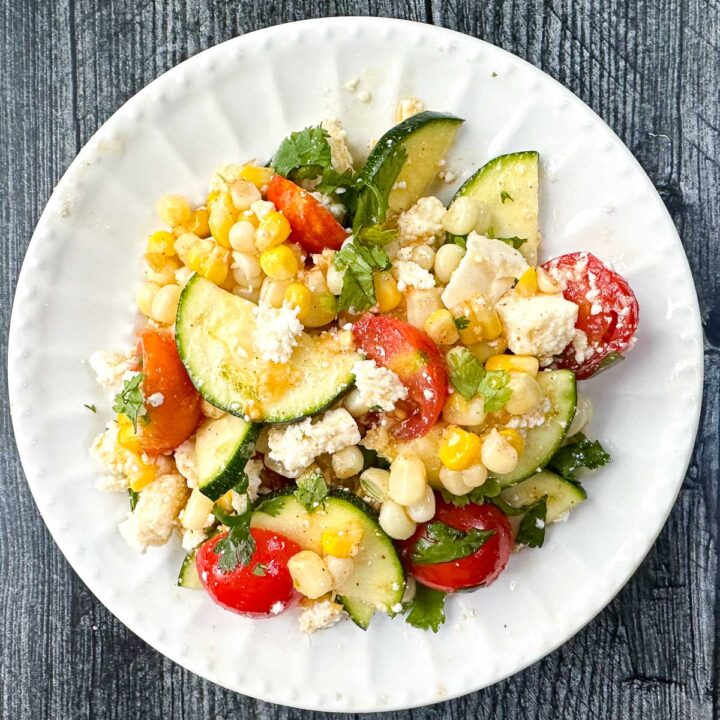 white plate with a zucchini corn and tomato salad