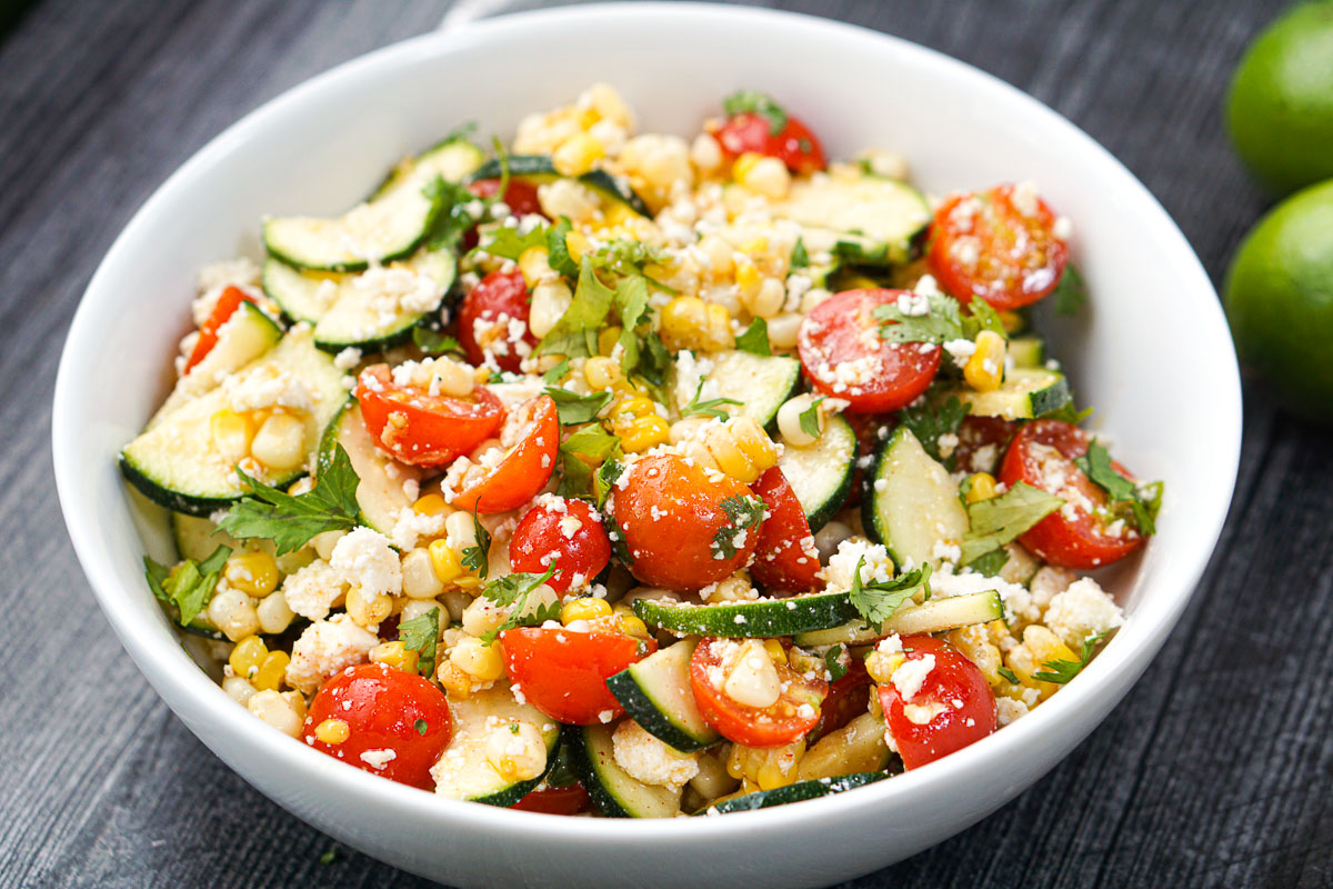 closeup of white bowl with garden zucchini, tomato and corn salad