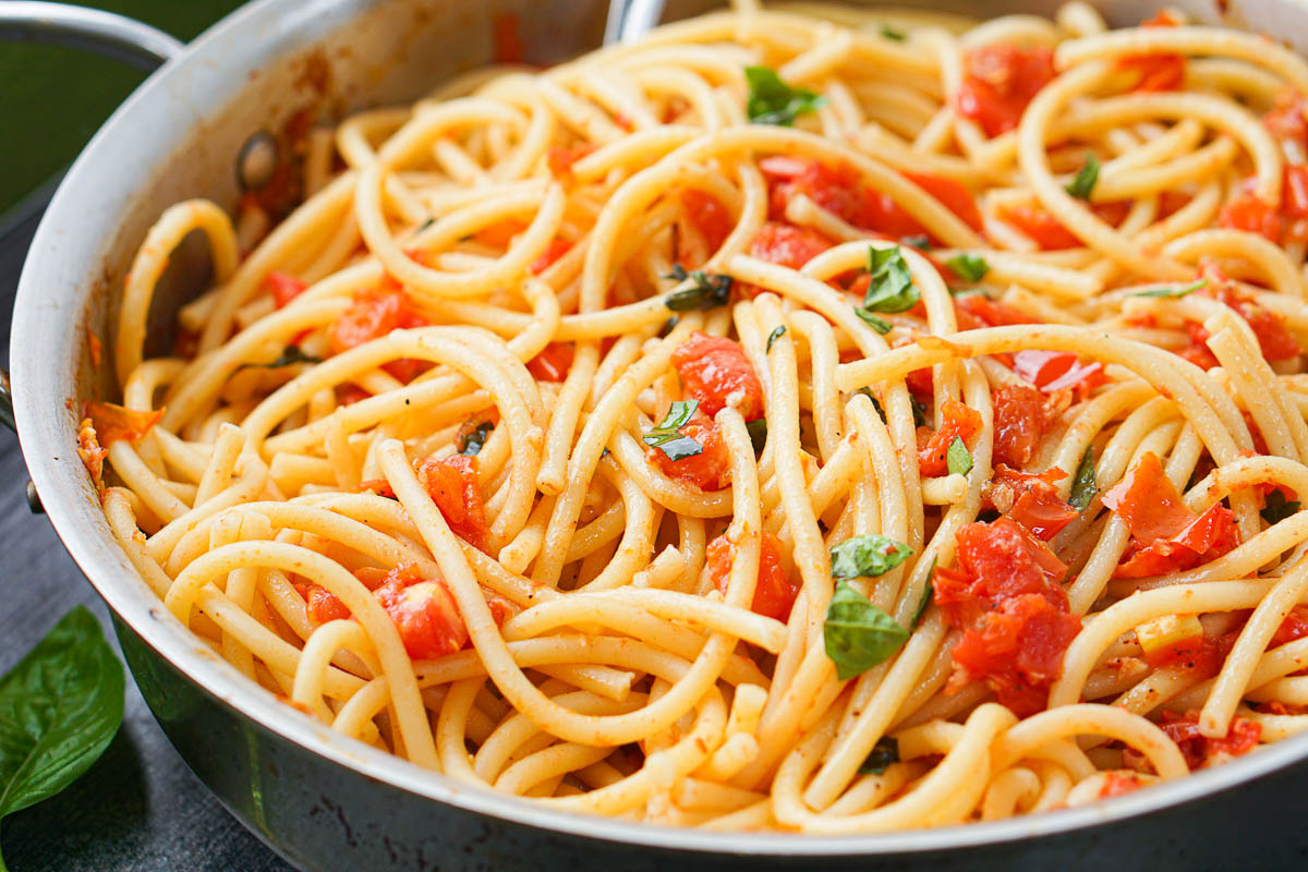 closeup of pan with pasta and fresh tomatoes and basil