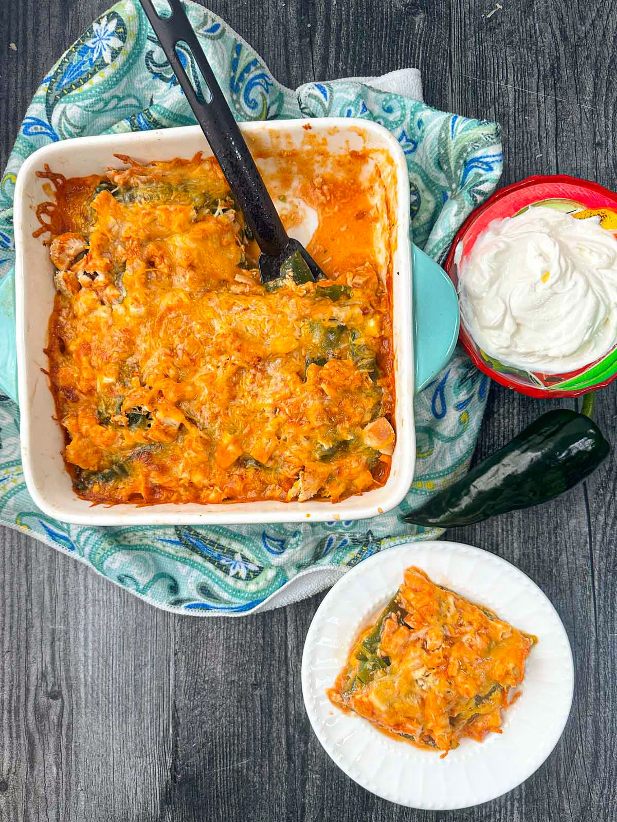 aerial view of baking dish and plate with chicken poblano casserole and sour cream