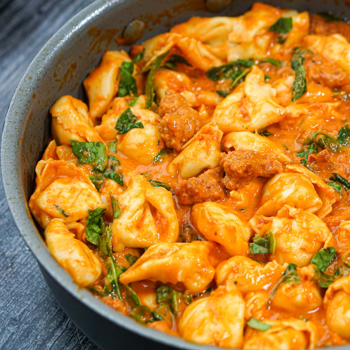 close up of a pan of tortellini with spinach and sausage sauce