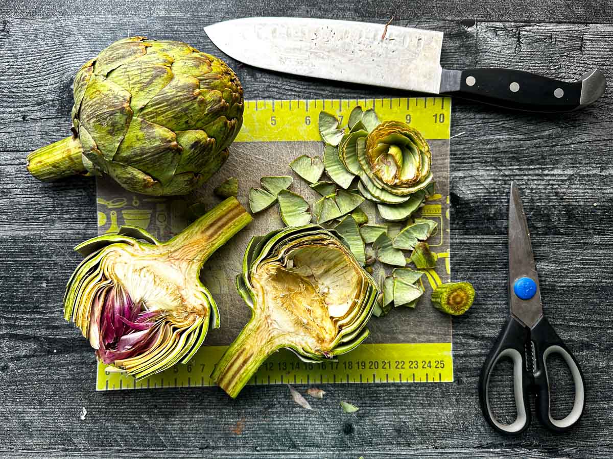 Cutting board with a cut and cleaned raw artichoke.