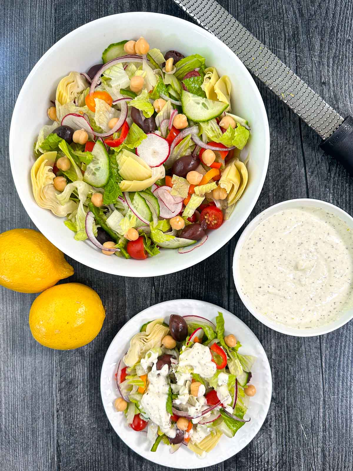 aerial view of a bow and plate with Greek salad and a bowl of creamy dressing and fresh lemons