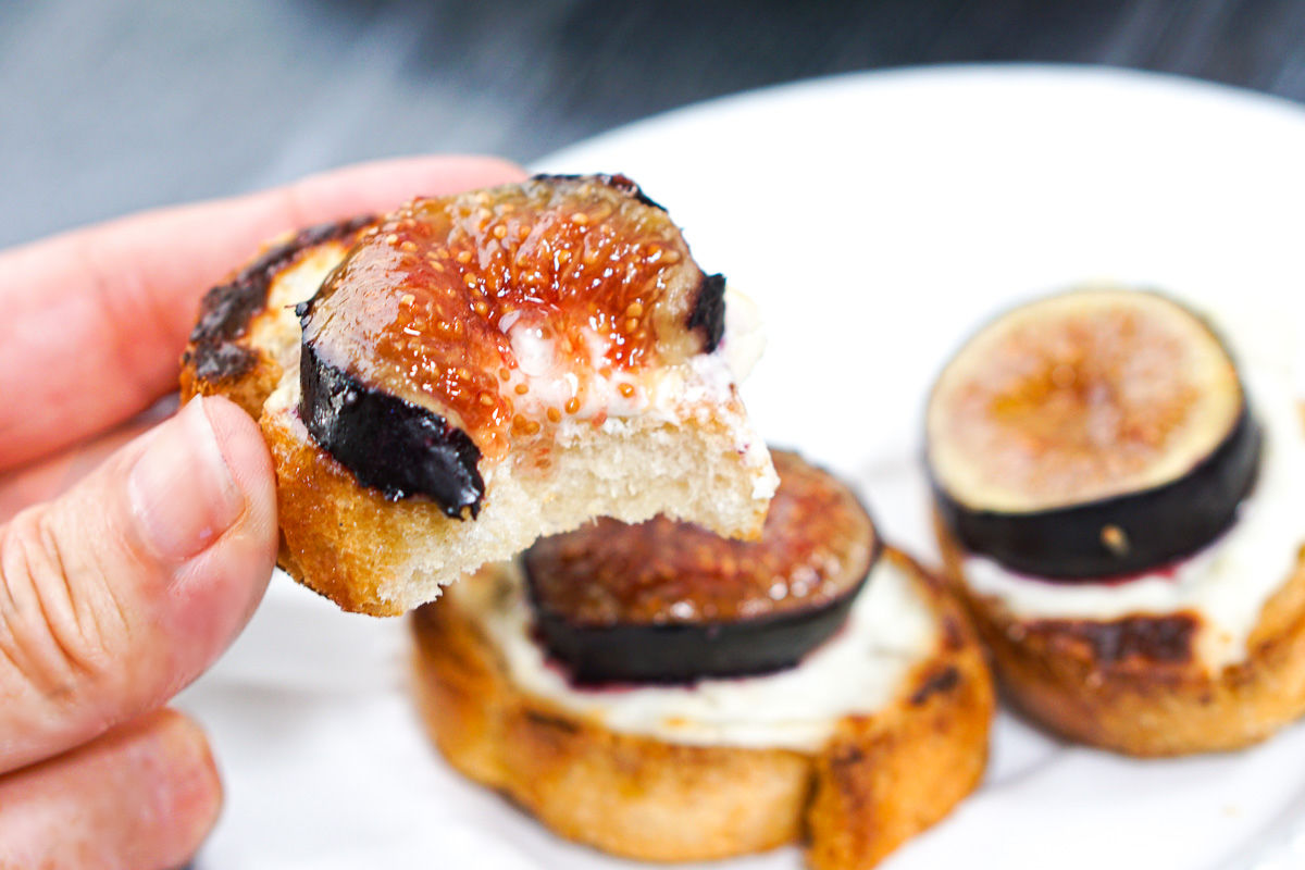 fingers holding a piece of crostini topped with blue cheese and fig with a bite taken out