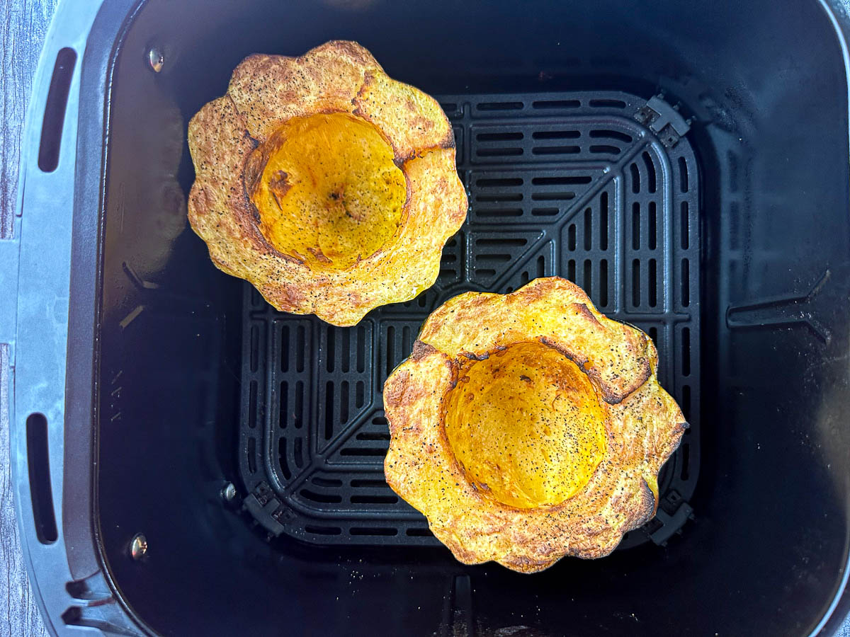 air fryer basket with 2 halves of acorn squash baked
