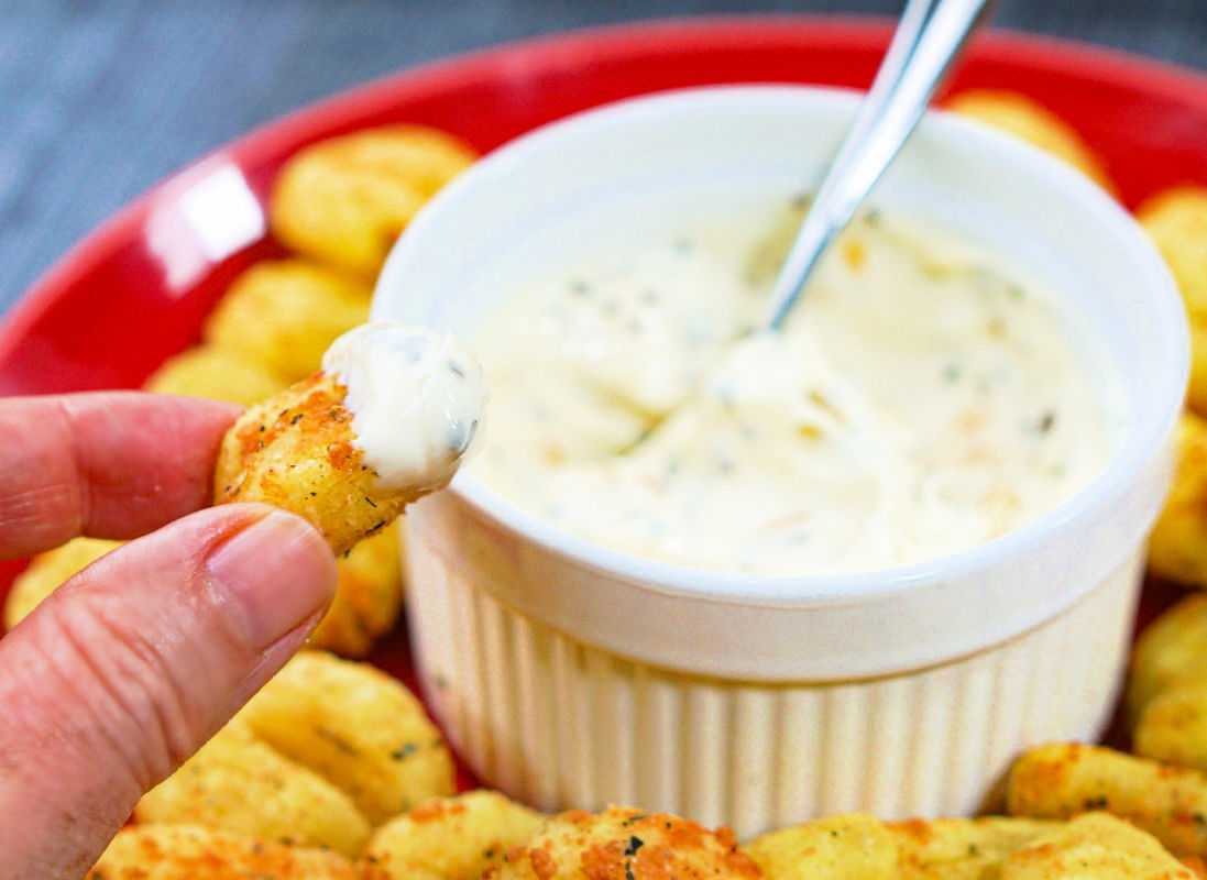 fingers holding fried piece of gnocchi with dip on it