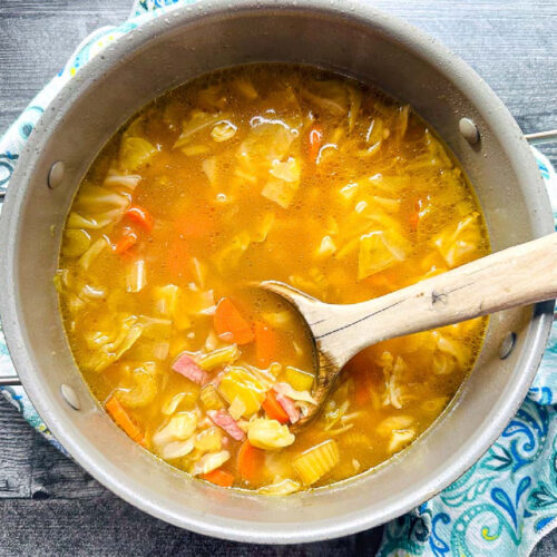 Aerial view of a pot of ham and cabbage soup with wooden ladle.