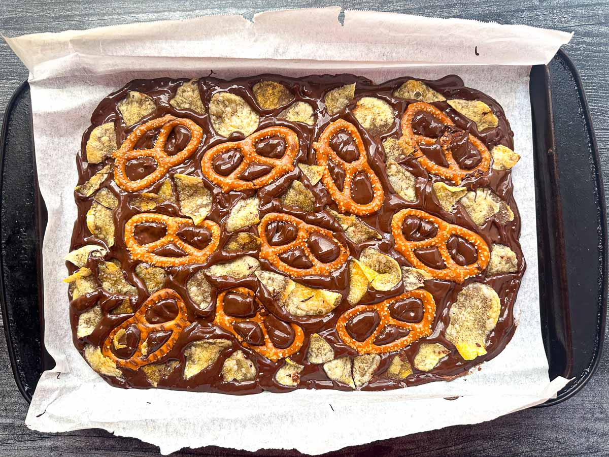 baking tray with melted chocolate with potato chips and pretzels in it ready to freeze