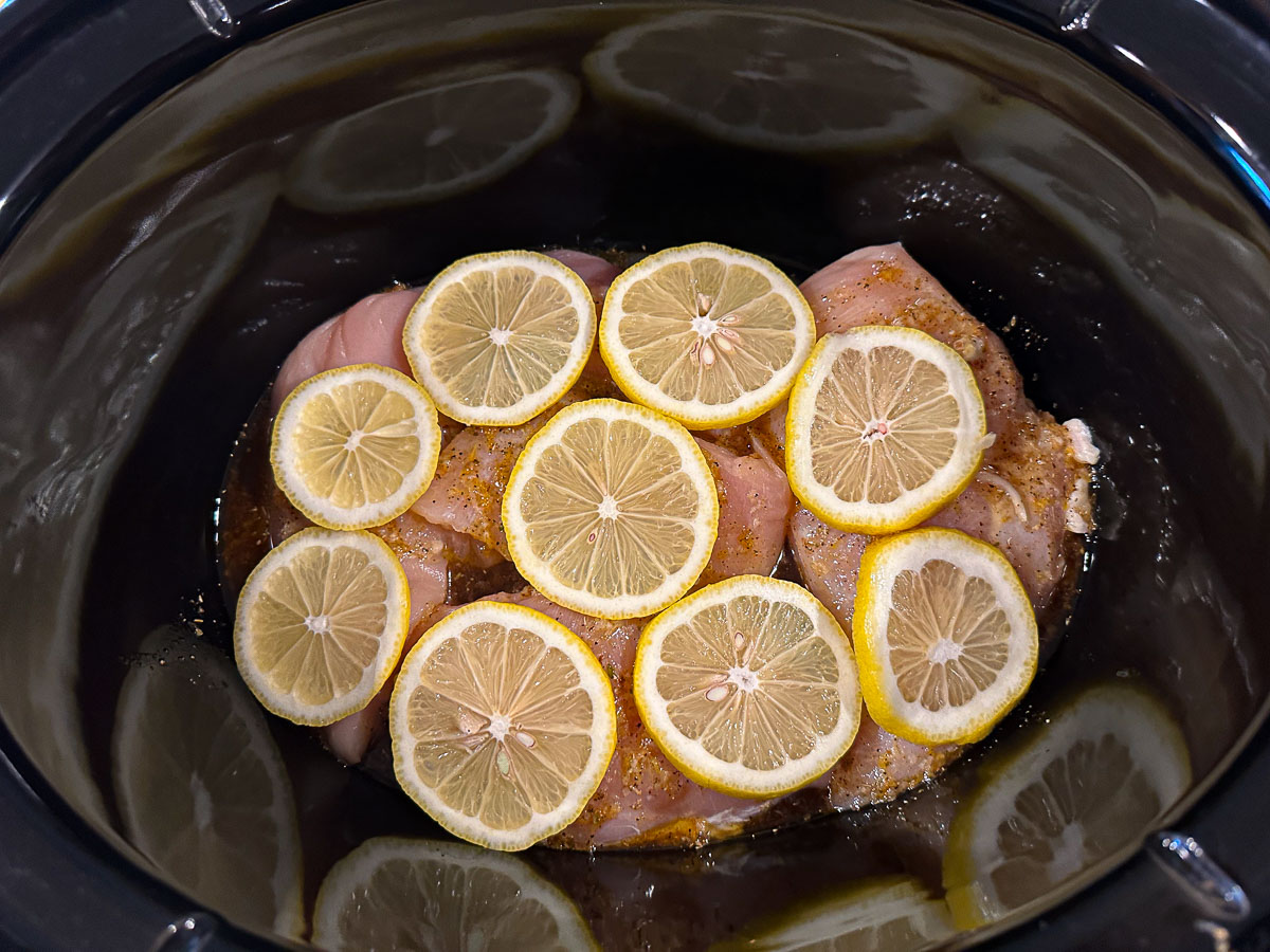 black crock with chicken and lemons ready to bake