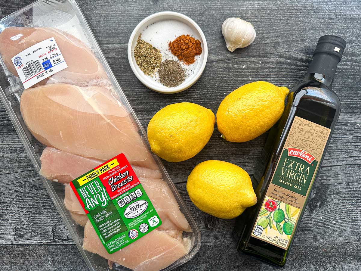 recipe ingredients - raw chicken breasts, lemons, spices, olive oil and garlic