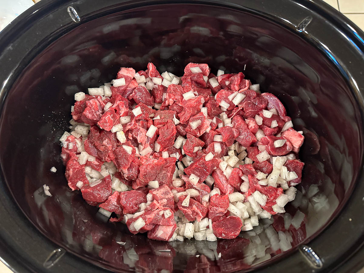 crock pot with raw lamb pieces and onion