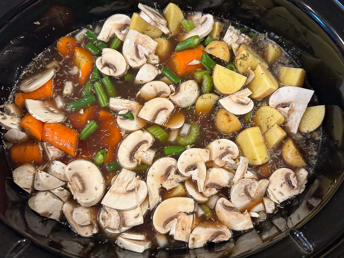 slow cooker with veggies and broth and seasonings ready to cook