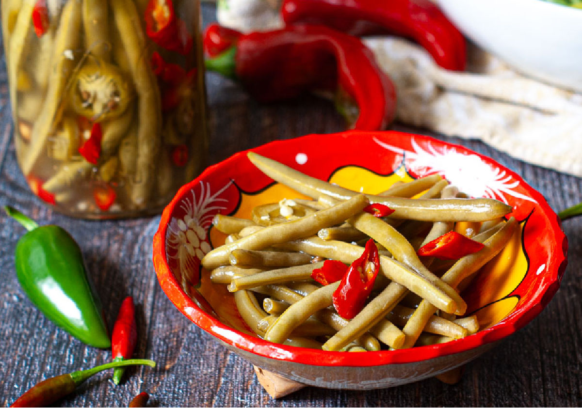 Closeup of a red bowl with pickled green beans with red and green peppers.