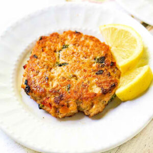 white plate with keto salmon cake made from leftover salmon and wedges of lemon
