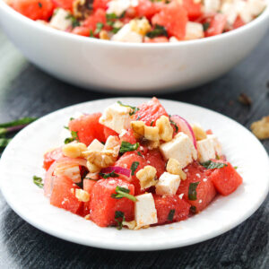 white plate with a serving of watermelon salad with feta and walnuts