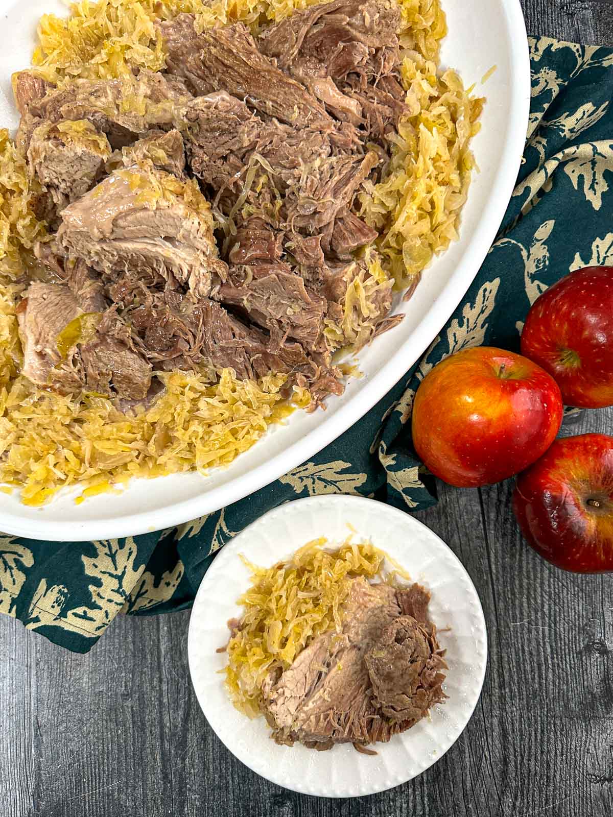 Aerial view of a platter and plate with pork and sauerkraut made in the instant pot and some fresh apples.