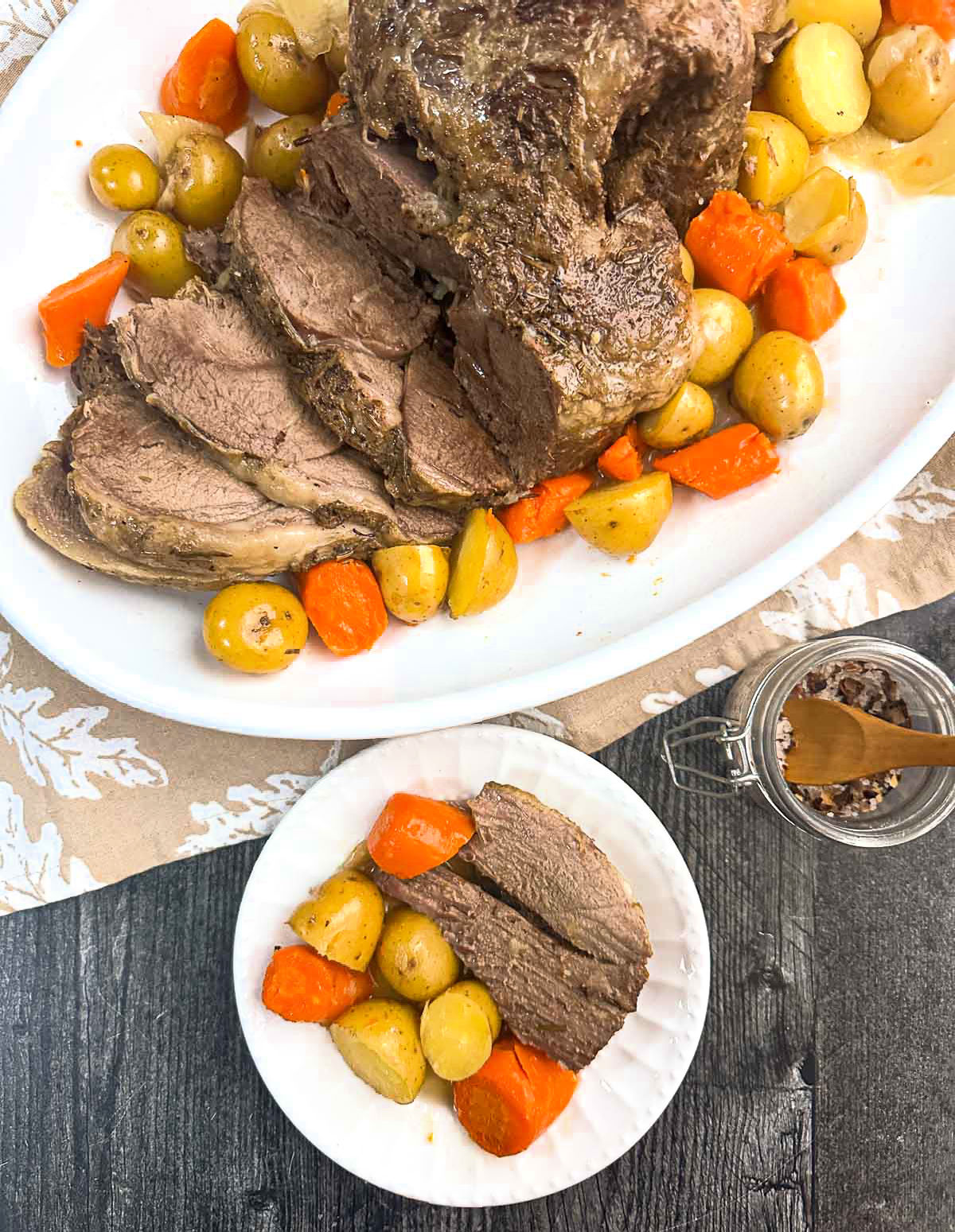 Aerial view of a white platter and plate with leg of lamb roast with carrots and potatoes made in the Instant Pot.