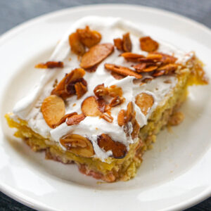 A white plate with a piece of gluten free rhubarb cake with candied almond slices on top.