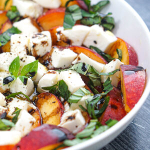 Closeup of a white bowl with peach caprese salad.