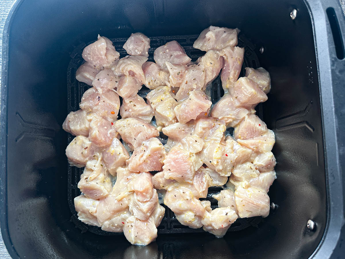 Air fryer basket with chunks of marinated chicken breast.