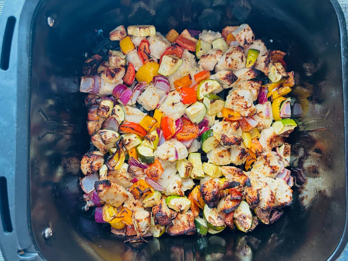 Air fryer basket with marinated chicken and veggies when done.