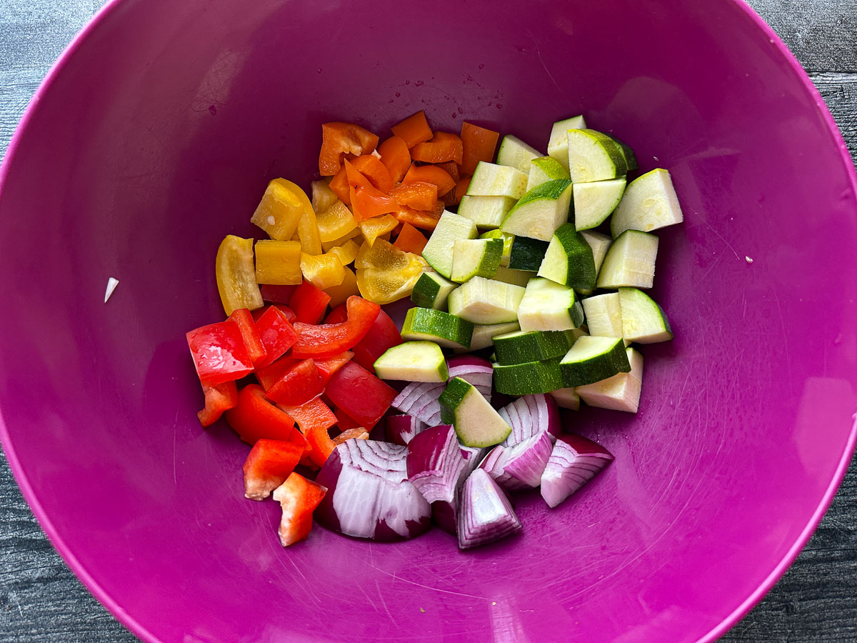 Purple bowl with chopped fresh vegetables - zucchini, red onion and peppers.