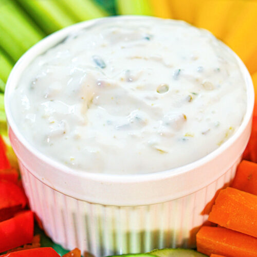 White bowl with keto cottage cheese pickle dip and veggies surrounding it.