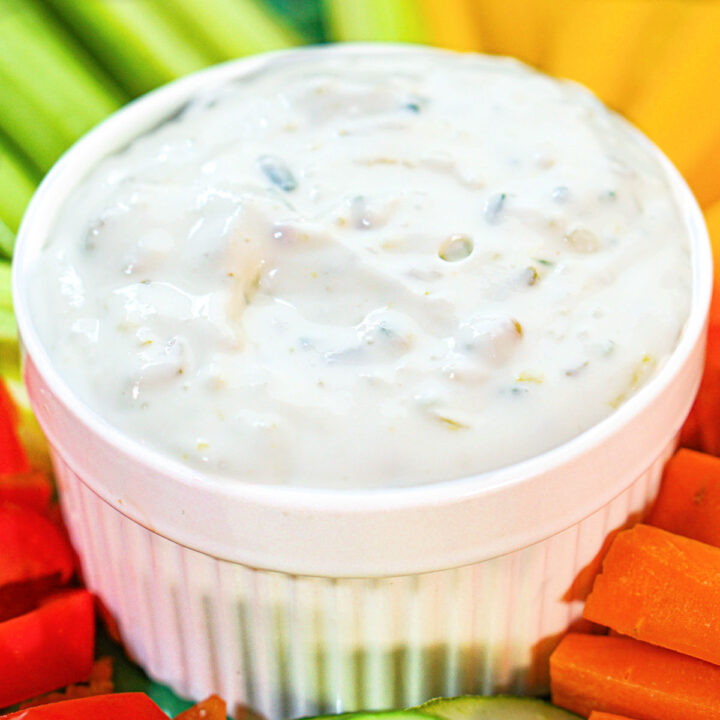 White bowl with keto cottage cheese pickle dip and veggies surrounding it.