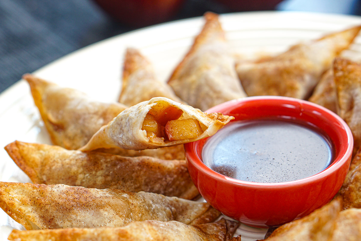 Closeup of an apple wonton with a bite taken out next to a bowl of brown sugar dip.