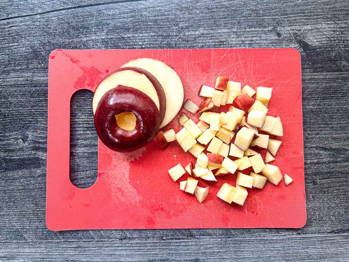 Red chopping board with chopped apples.