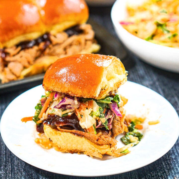 Closeup of a white plate with a bbq slider with a tray of them in the background.