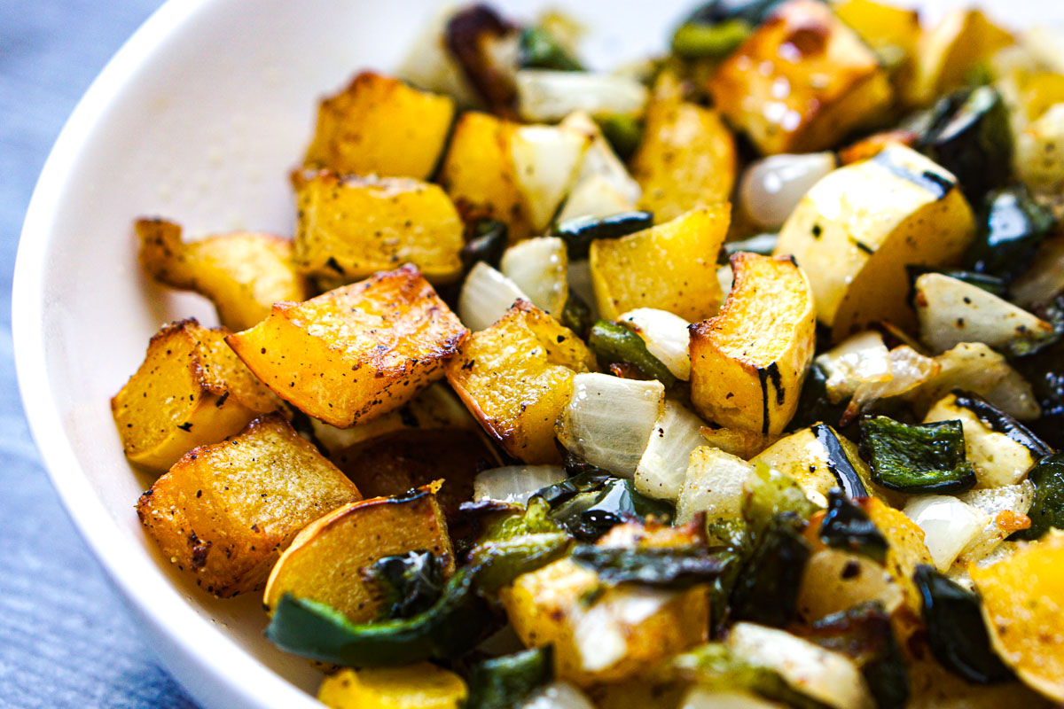 Close up of a white bowl with air fry delicata squash with peppers and onions.