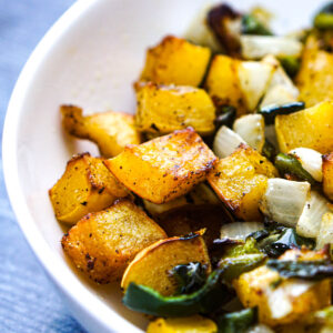 Close up of a white bowl with air fry delicata squash with peppers and onions.