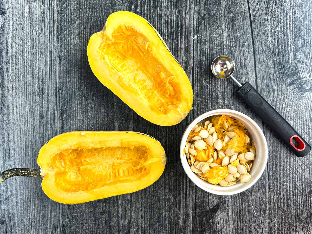 A delicata squash cut in half and with a. bowl of the seeds and a melon baller.