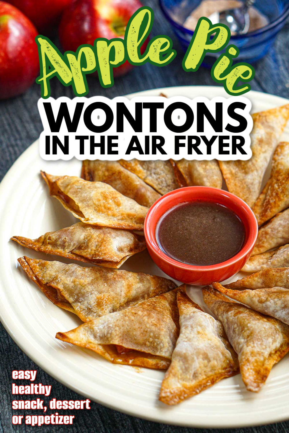 Closeup of a plate of the apple wontons with a a bowl of cinnamon brown sugar sauce and fresh apples and cinnamon sugar and text overlay.