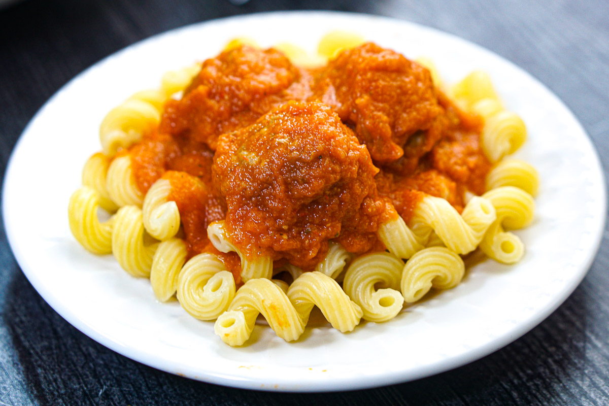 White plate with noodles and finished sauce with meatballs.
