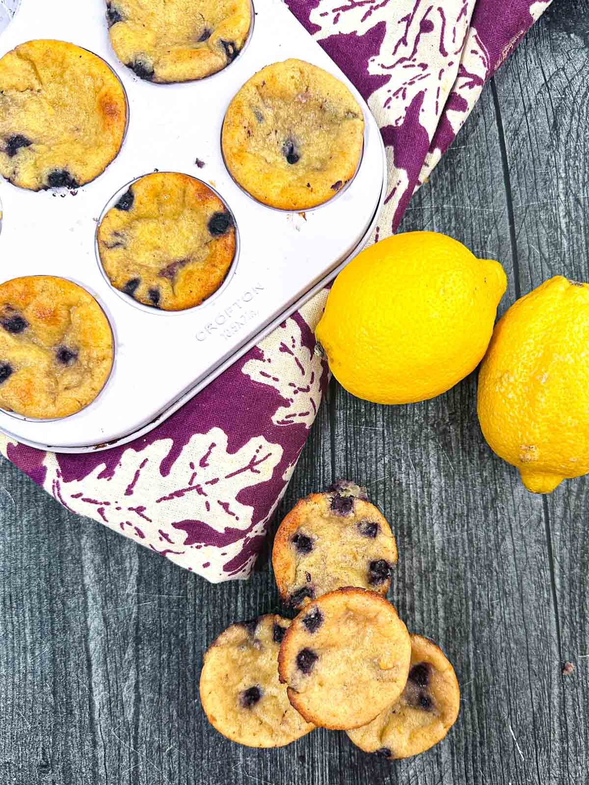 Aerial view of keto cottage cheese blueberry muffins with fresh lemons and a purple tea towel.